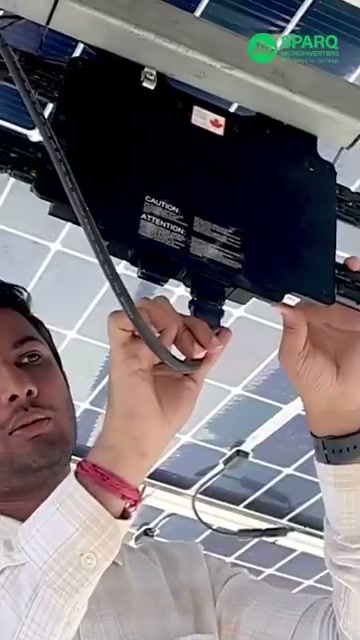 An installer connects a Quad microinverter under a solar panel on a live site